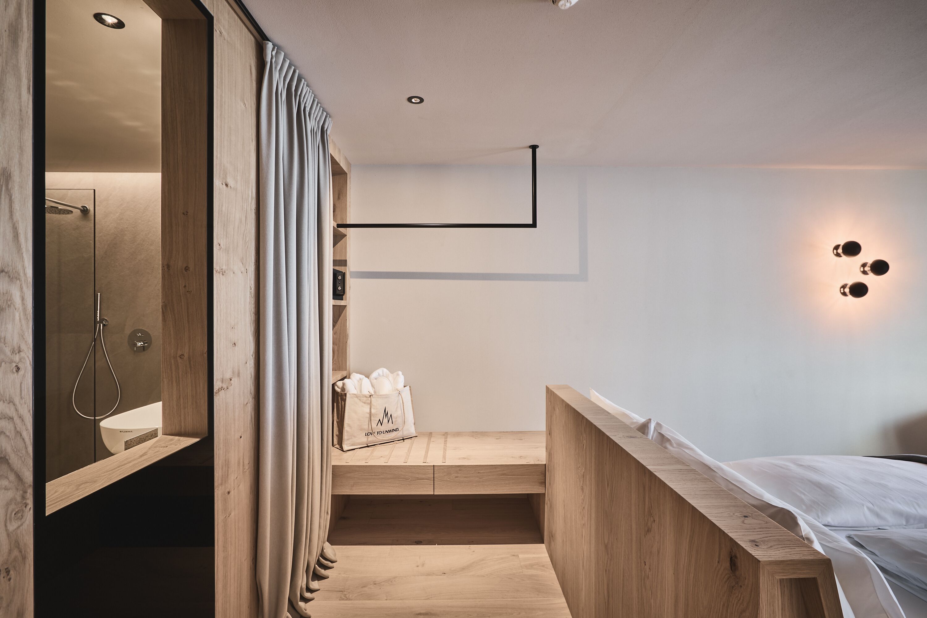 Ein modernes Hotelzimmer mit Holzboden, einem Bett, einem kleinen Schreibtisch und einer Dusche.