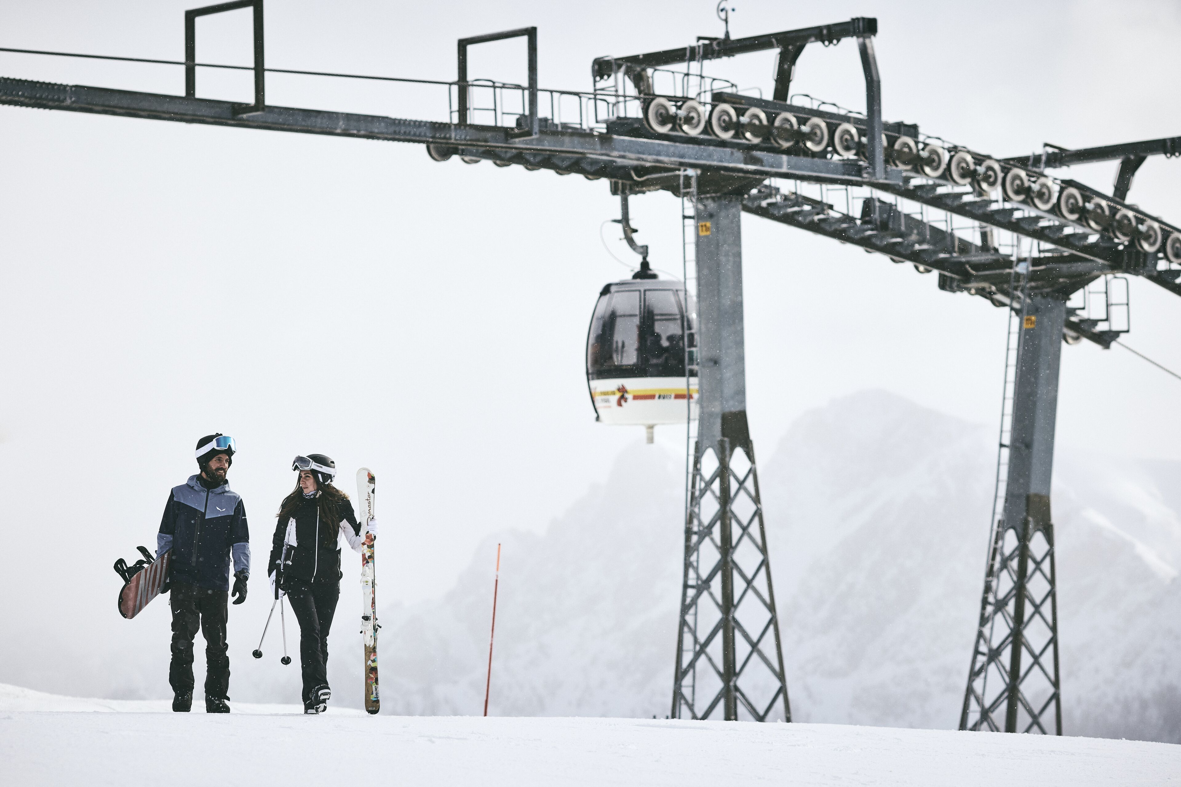 Un telesilla con cabina, una torre metálica y una montaña nevada al fondo.