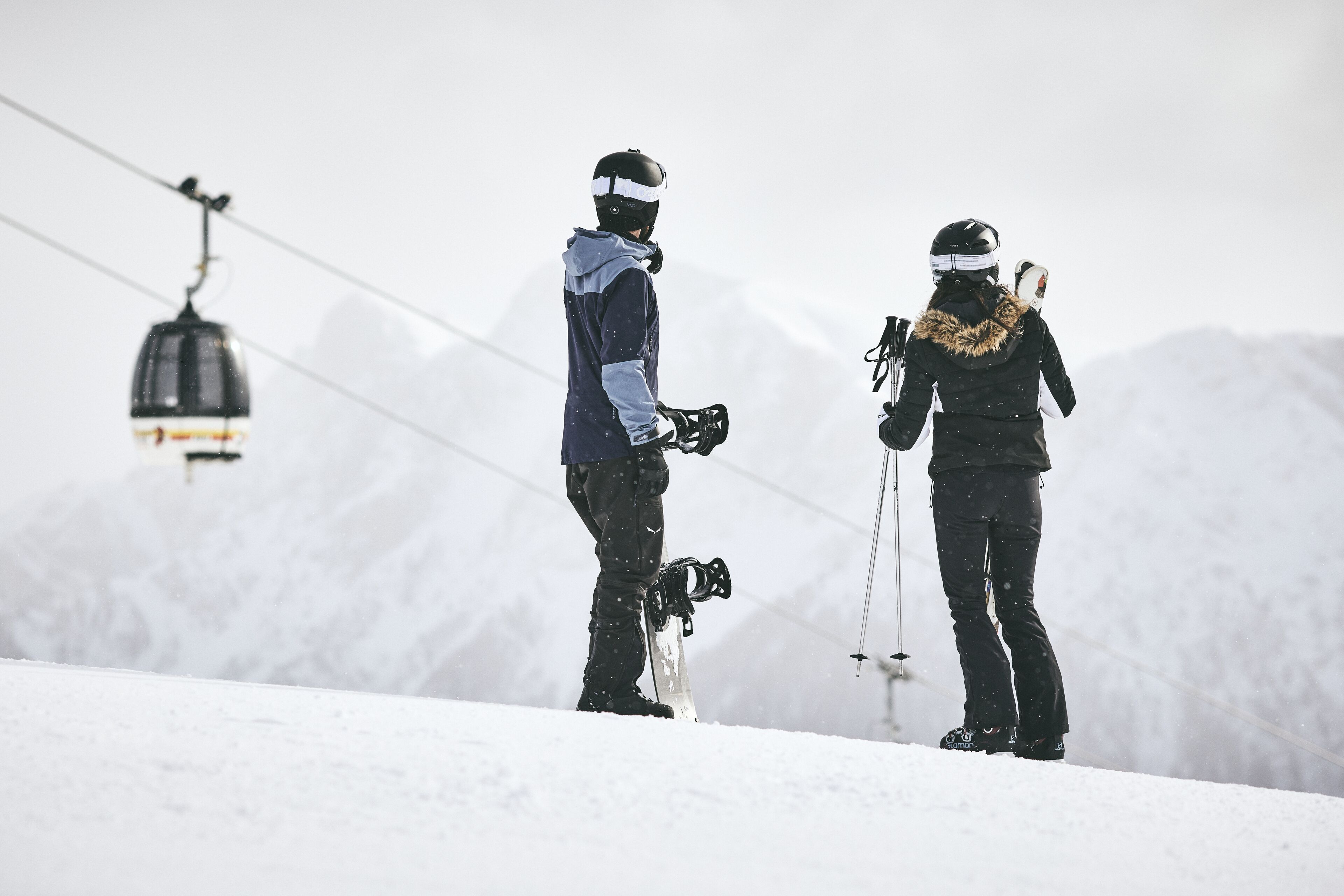 Two skiers on a snowy slope with a ski lift in the background.