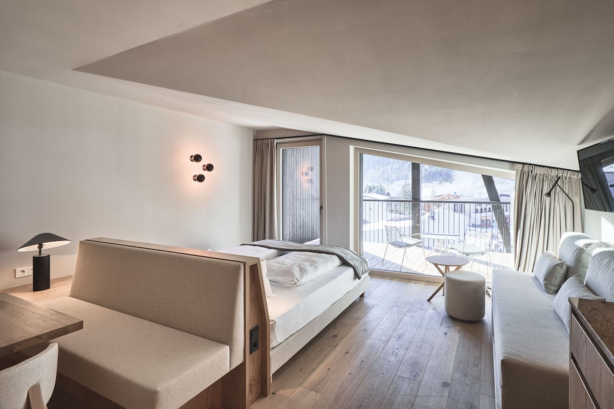 Ein modernes Hotelzimmer mit Bett, einer Sitzecke, einem kleinen Tisch und Blick ins Freie.