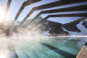 A clear pool with a view of snow-covered mountains and a wooden structure in the background.