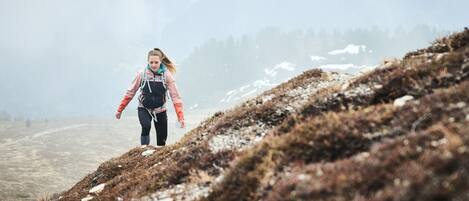A person walking on a rocky, hilly terrain with sparse vegetation and distant trees.