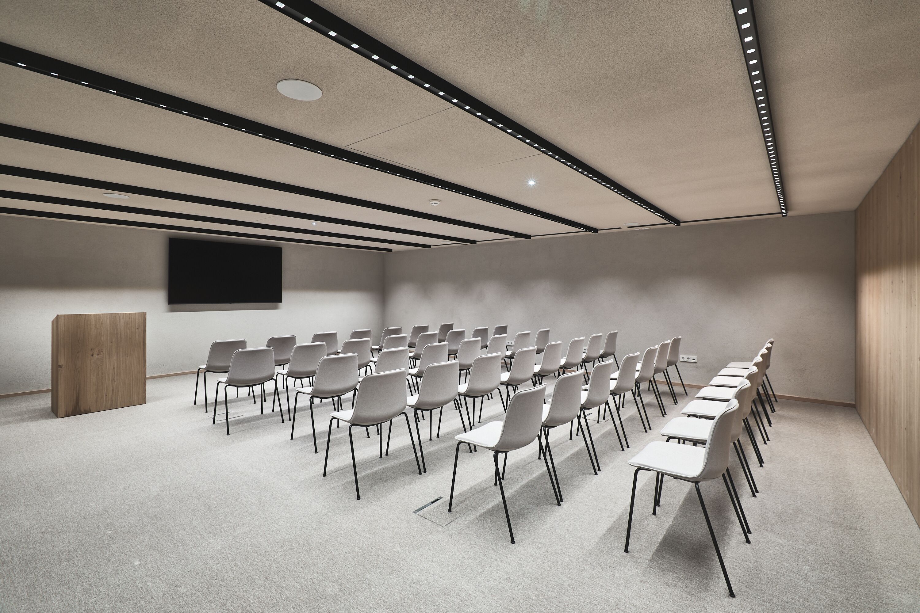 Ein Konferenzraum mit Reihen von Stühlen, einem Rednerpult und einer großen Leinwand an der Wand.