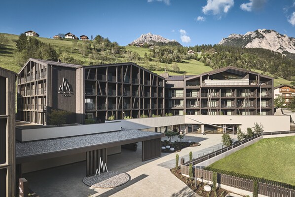 A modern hotel with a spacious courtyard, multiple balconies, and a view of mountains.