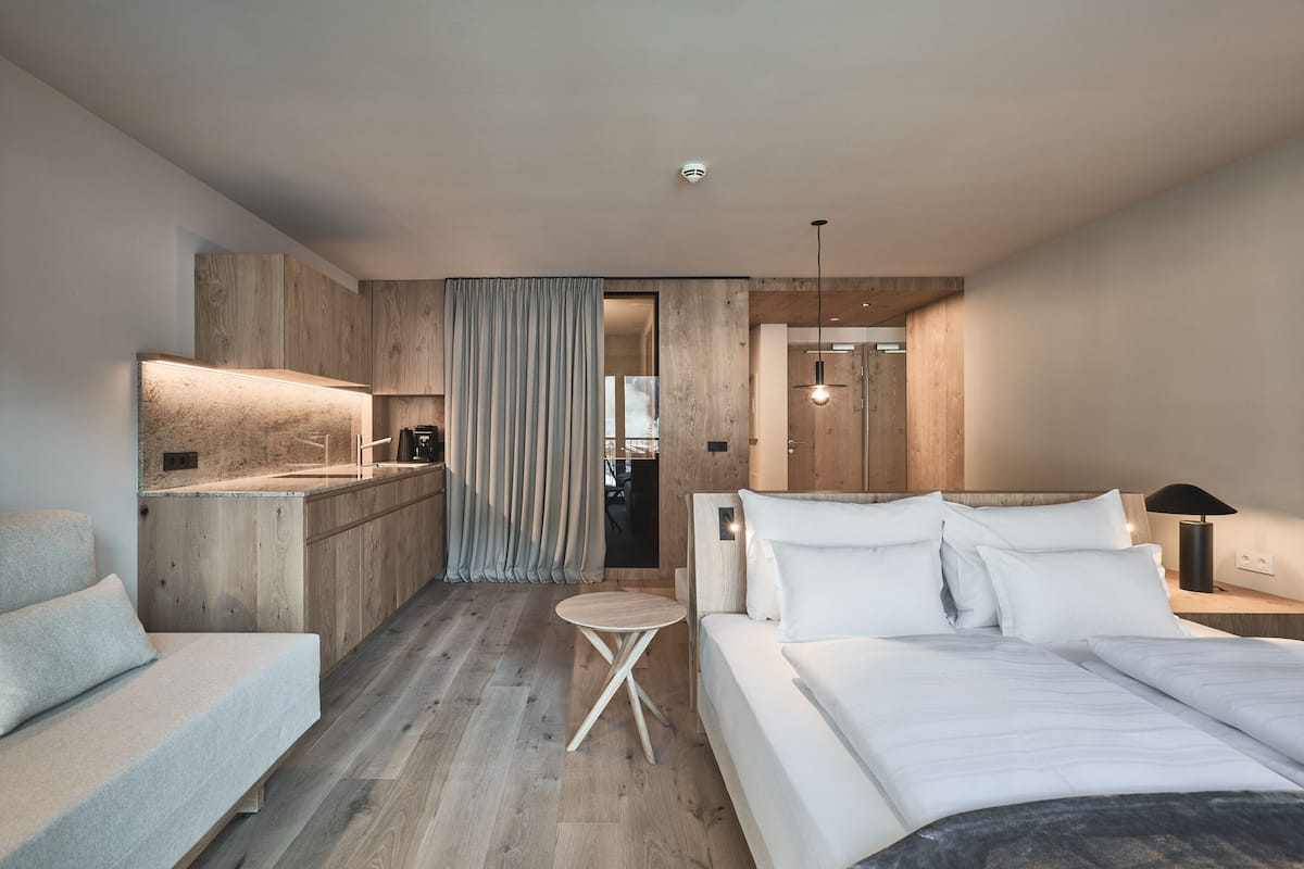 Ein modernes Hotelzimmer mit Holzboden, einem Bett mit weißen Leinen, einem kleinen runden Tisch und einer Küchenzeile.