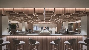 Una zona de bar moderna con una barra central, taburetes y un techo decorativo.