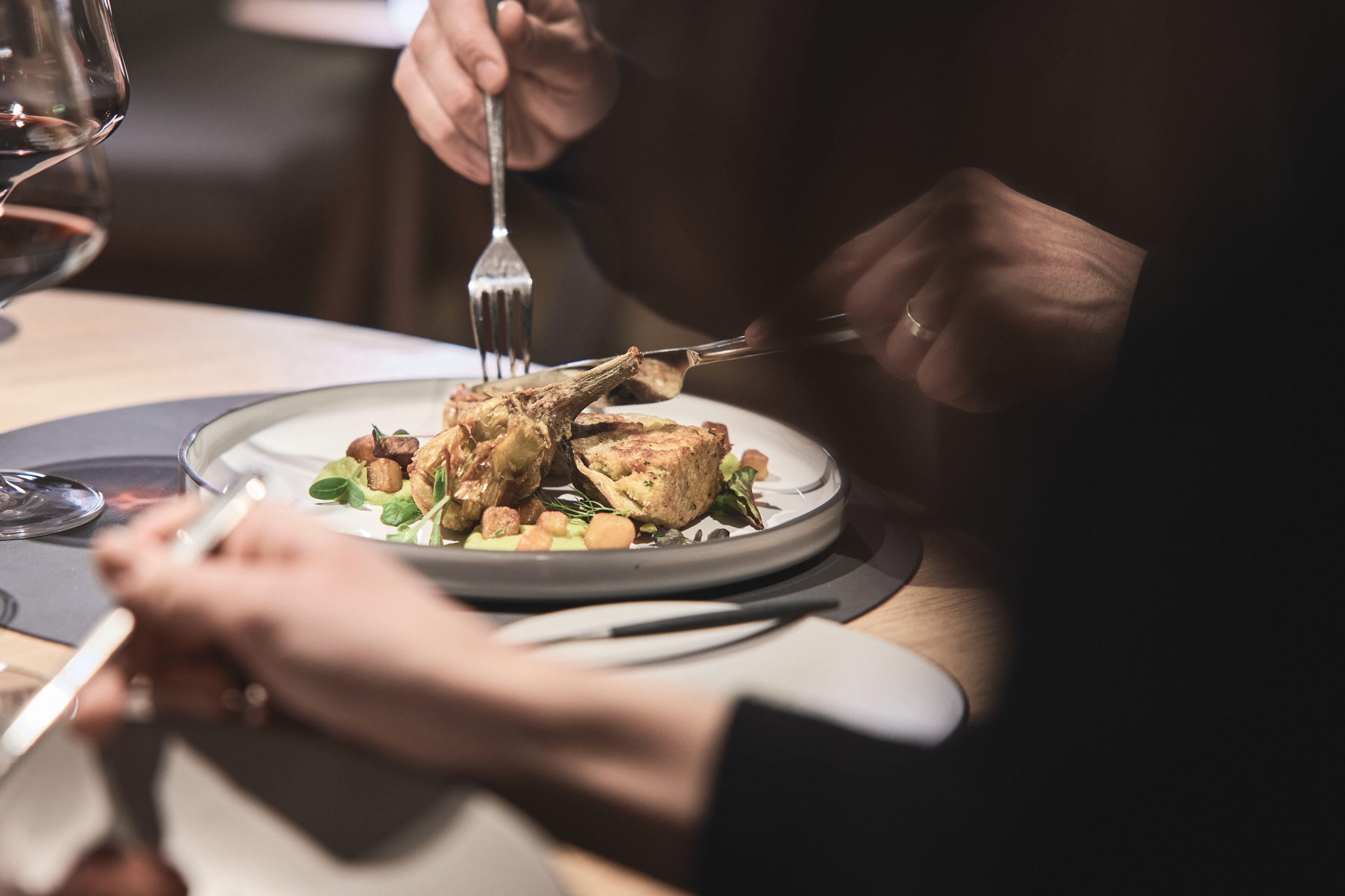 A dining table with a plate of food, a fork, and a glass of wine.