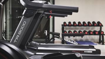 Un tapis de course TR 8000 avec un banc de musculation et des haltères en arrière-plan.