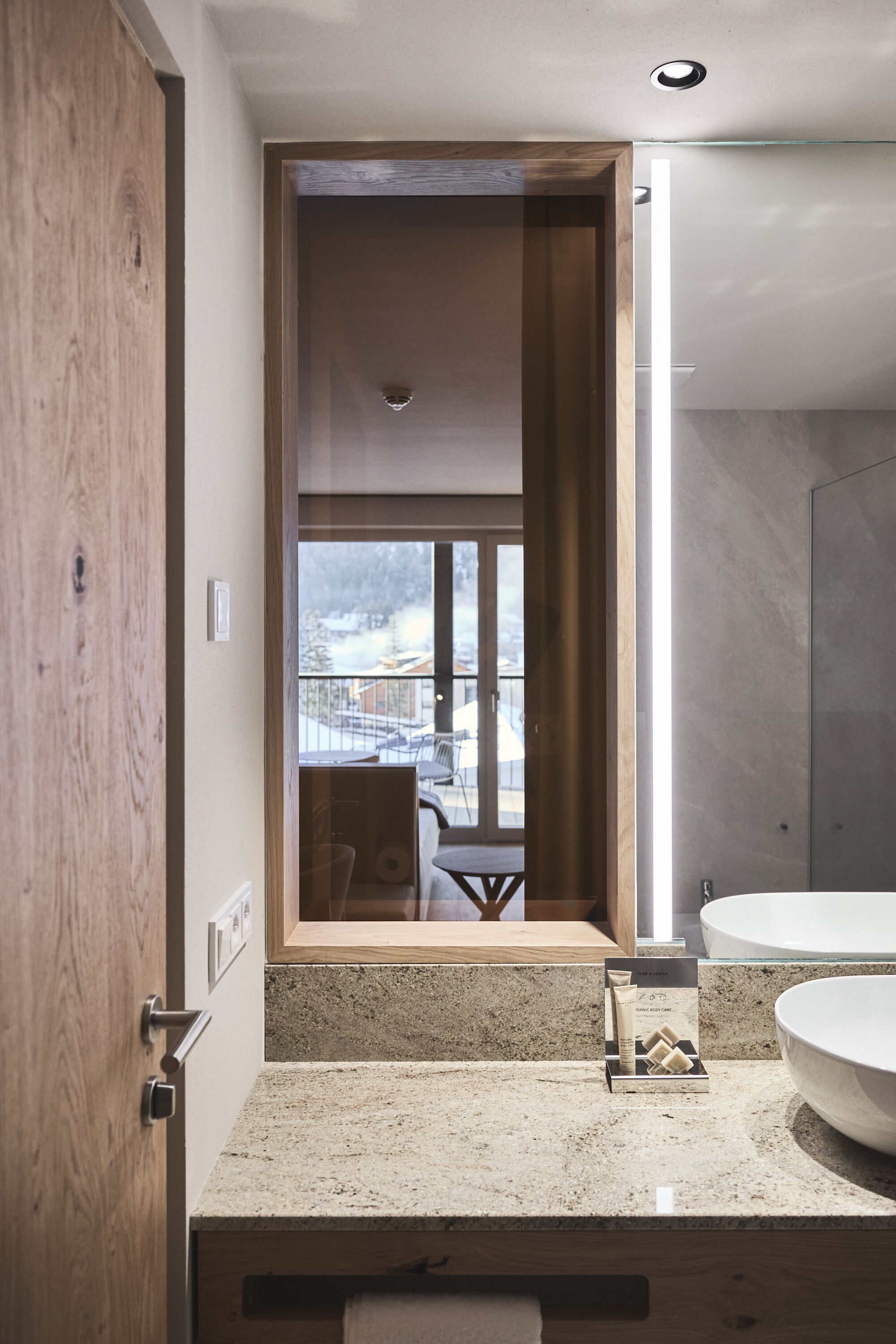 Een moderne badkamer met een groot raam, een houten deur en een granieten aanrechtblad.