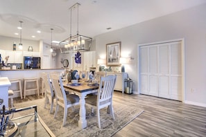 A modern kitchen with white cabinetry, a dining table set for four, and a large window with blinds. - New! Elegant Waterfront Charmer ~ 402 Island Key (Clearwater)
