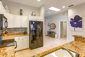 A modern kitchen with white cabinets, a stainless steel refrigerator, granite countertops, and a large window.