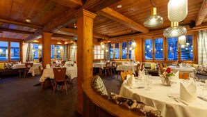 Un restaurante con interiores de madera, varias mesas preparadas para comer y grandes ventanales con vistas.