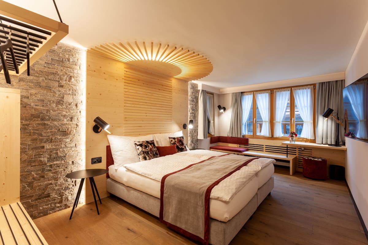 A modern bedroom with a large bed, wooden accents, stone wall, and large windows.
