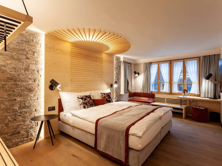 A modern bedroom with a large bed, wooden accents, stone wall, and large windows.