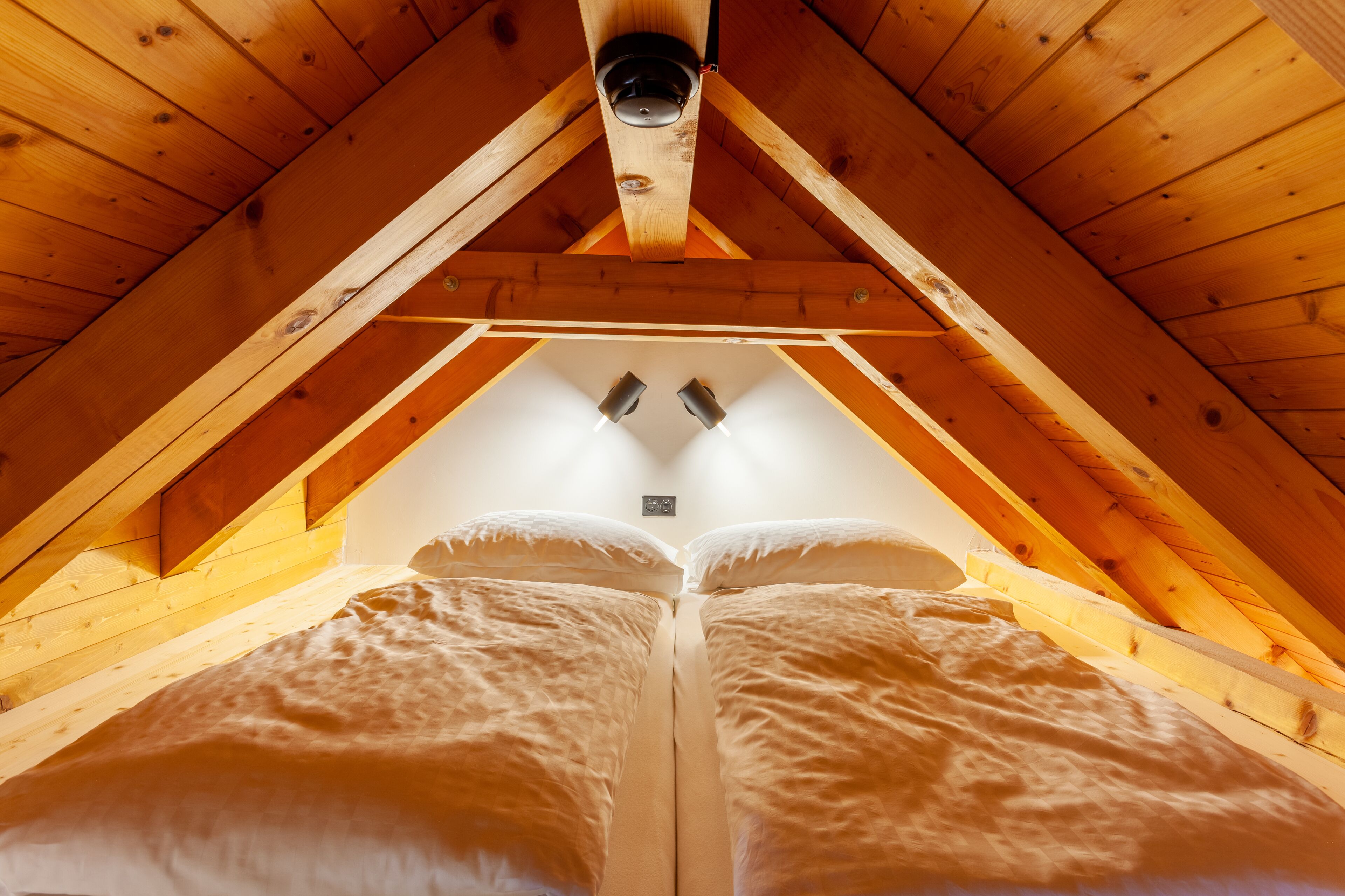 A cozy attic bedroom with a sloped ceiling, wooden beams, and a central light fixture.