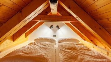 A cozy attic bedroom with a sloped ceiling, wooden beams, and a central light fixture.