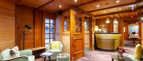 Una habitación acogedora con paredes y techo de madera, una recepción y zonas de estar con un banco y sillas.