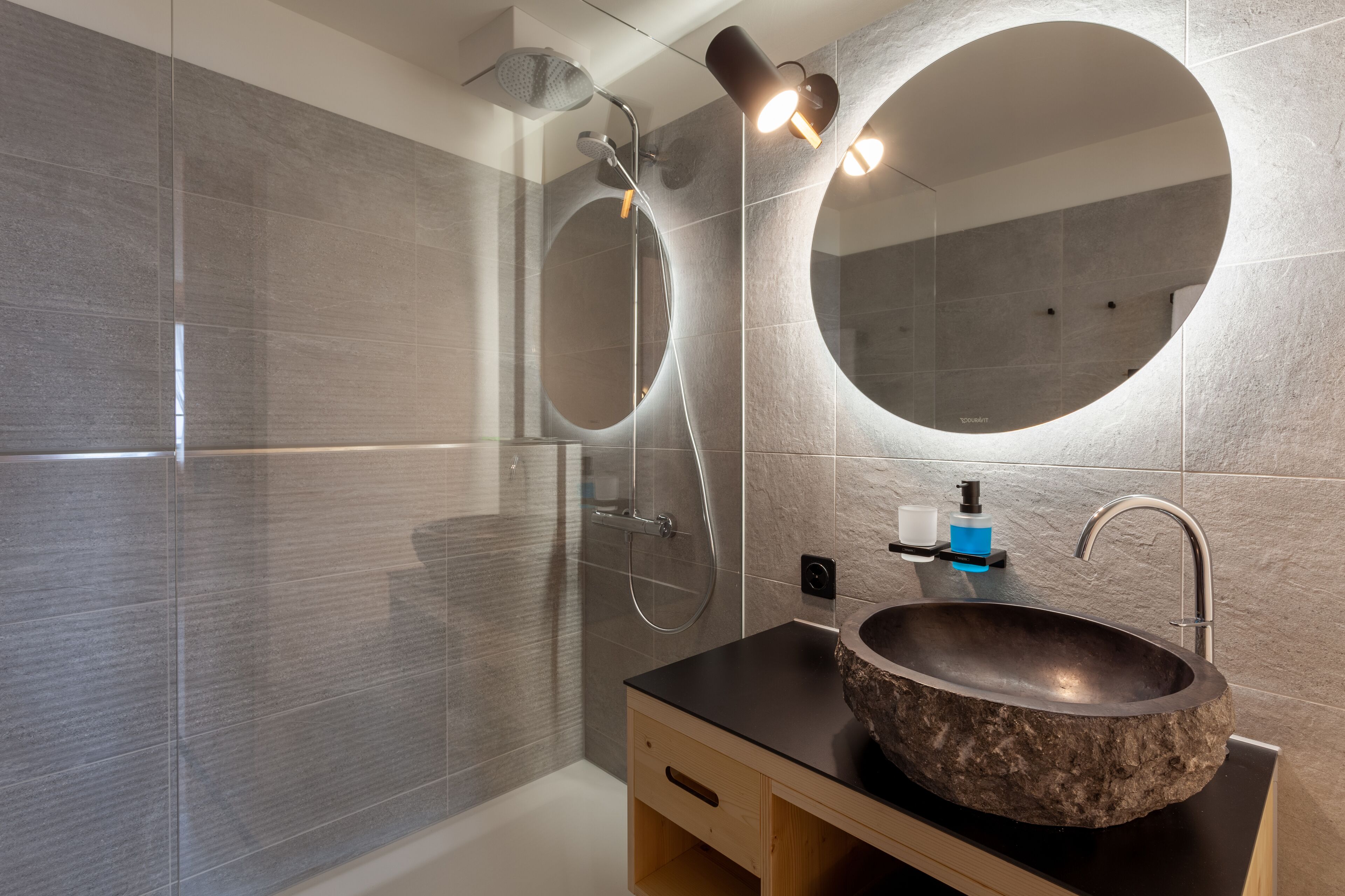 A modern bathroom with a stone sink, a large mirror, and a glass-enclosed shower.