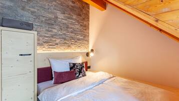Une chambre avec un mur en pierre, un plafond en bois et un lit avec une literie blanche et rouge.