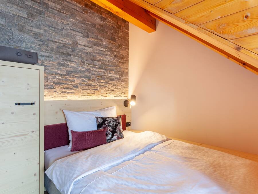Une chambre avec un mur en pierre, un plafond en bois et un lit avec une literie blanche et rouge.