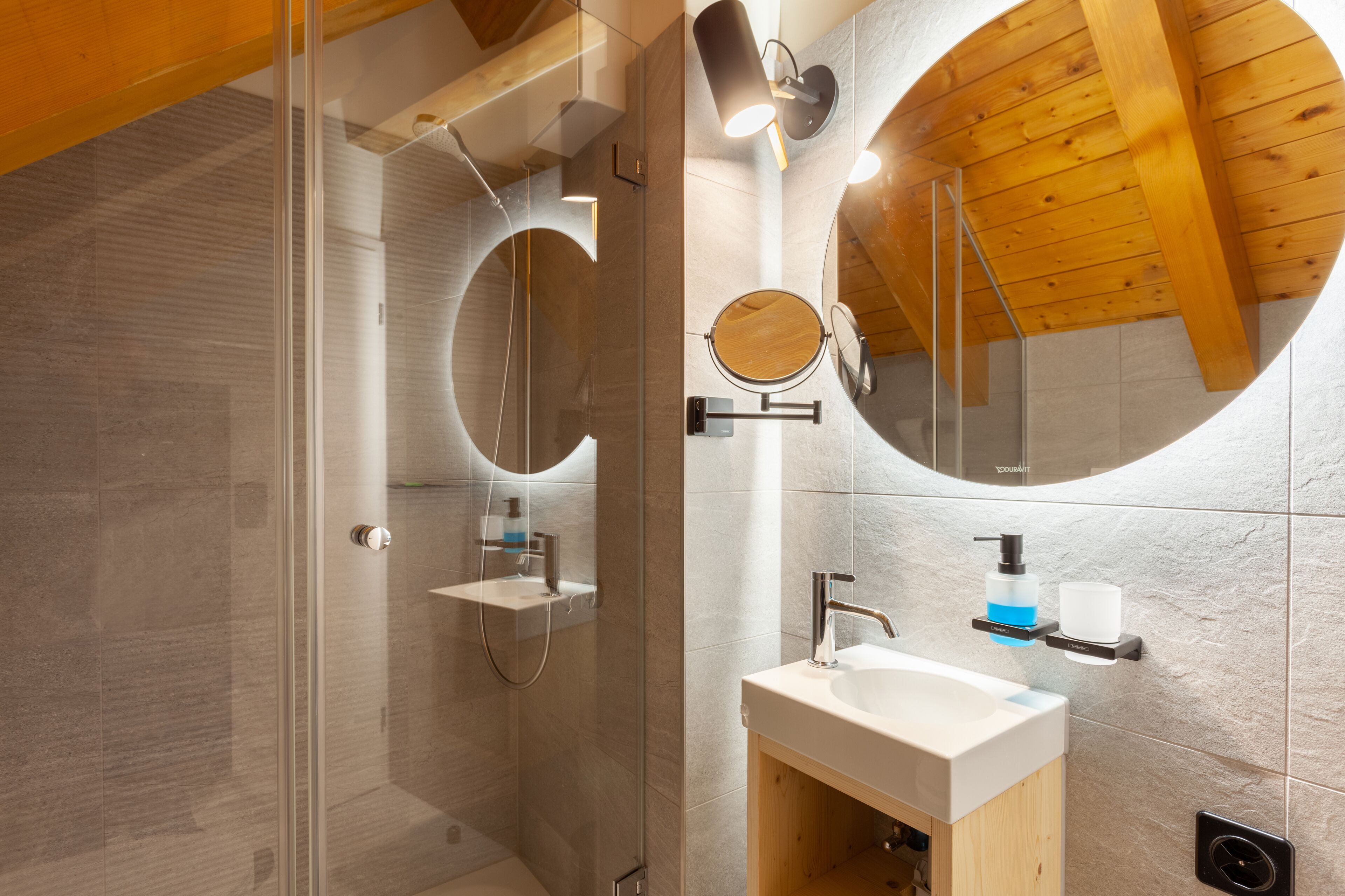 Une salle de bain moderne avec une douche à l’italienne en verre, un plafond en bois et un grand miroir au-dessus du lavabo.