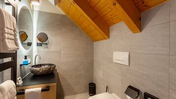 Un baño moderno con techo de madera, lavamanos de piedra, inodoro y perchero para toallas.