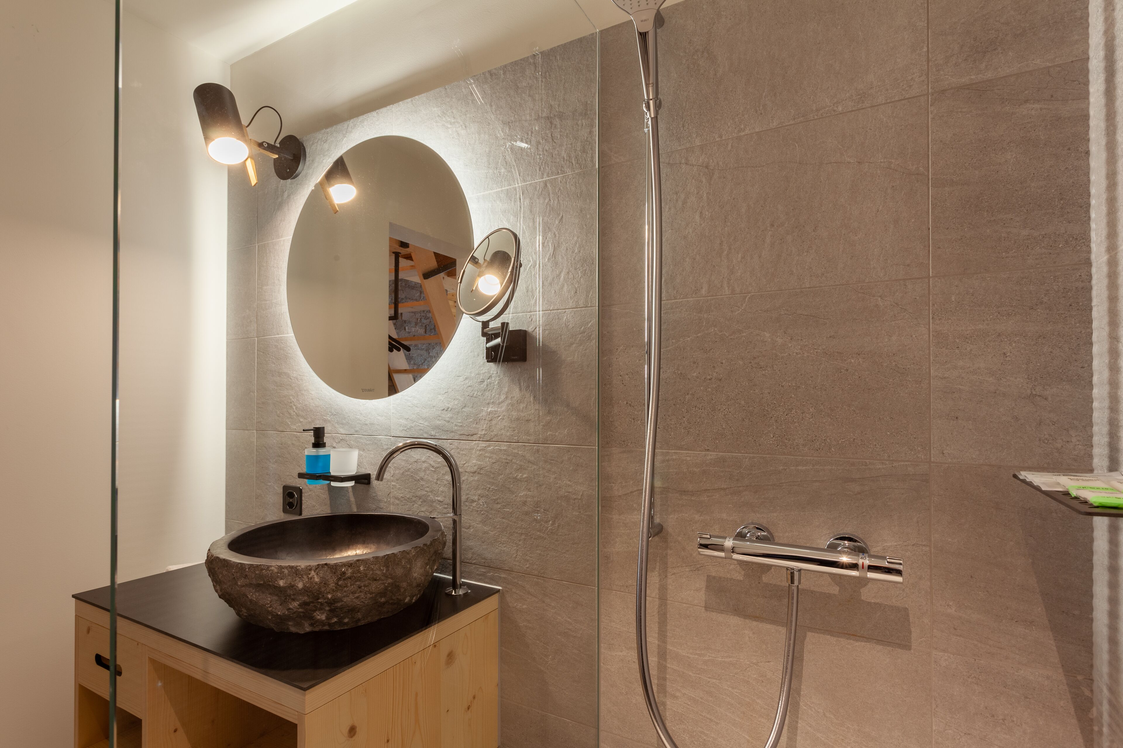 Une salle de bain moderne avec un lavabo en pierre, un miroir rond et une cabine de douche en verre.