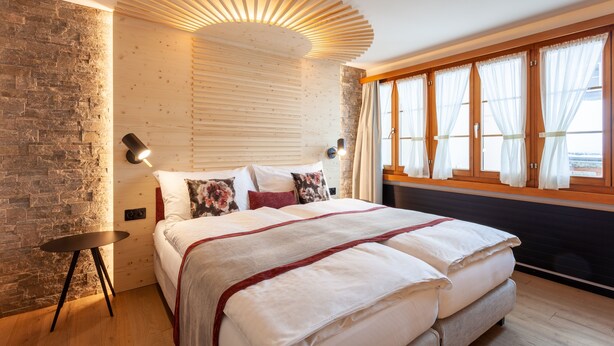 Un dormitorio moderno con una cama grande, cabecera de madera, pared de acento de piedra y una ventana con cortinas.