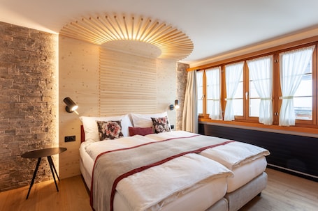A modern bedroom with a large bed, a wooden headboard, a stone accent wall, and a window with curtains.