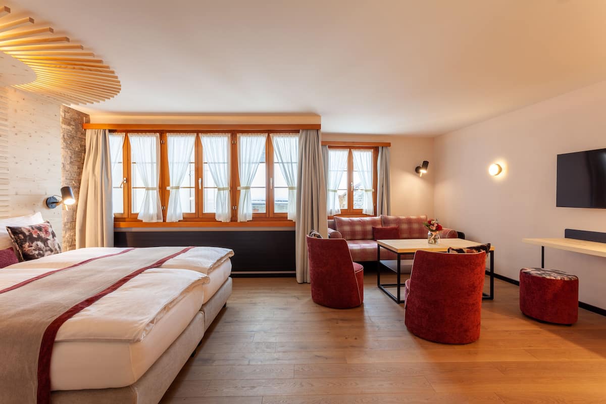 A hotel room with a bed, a sofa, a dining table, and a TV.