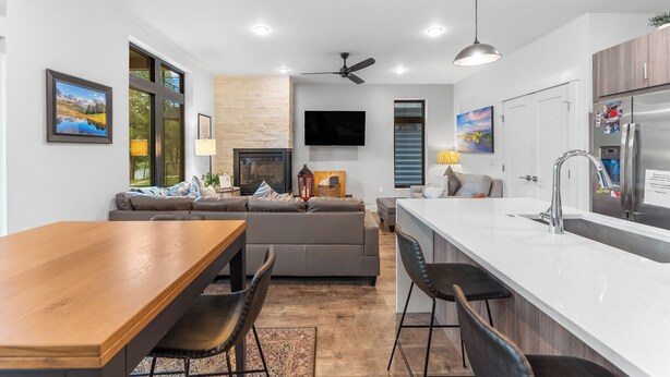 A modern kitchen with a central island, a dining area with a wooden table, and a living area with a sofa and a fireplace. - River West Condos #714 by Summit County Mountain Retreats (Silverthorne)