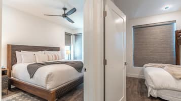 A bedroom with a bed, a nightstand, a ceiling fan, a window with blinds, and a door.