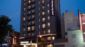 Een hoog hotel met meerdere verdiepingen, verlichte ramen en een opvallend bord waarop staat dat het een hotel is dat 24 uur per dag open is.