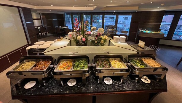 Een buffetopstelling met meerdere foodstations, een bloemenstuk als decoratie en een uitzicht op de stad door grote ramen.