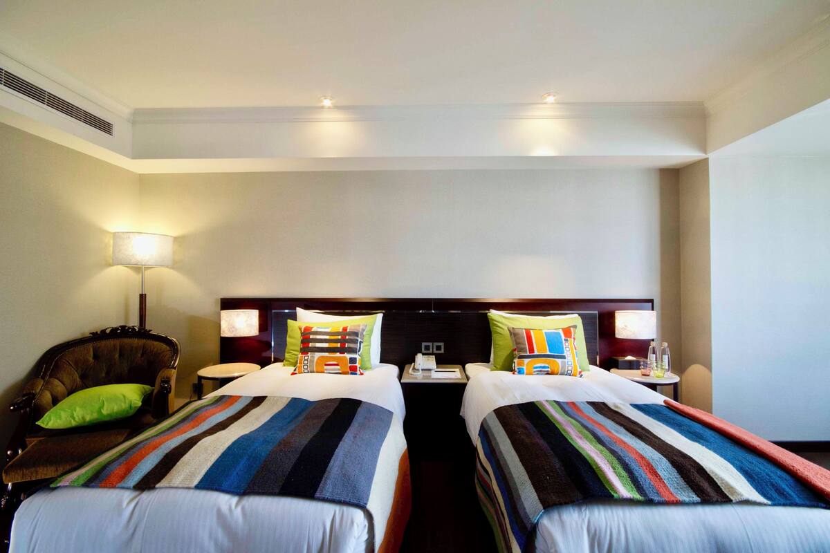 Ein Hotelzimmer mit zwei Betten, einem Sessel, einem Nachttisch und einer Lampe.