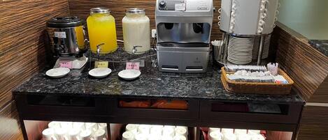Uma estação de bebidas com serviço próprio, incluindo máquinas de café, dispensadores de suco e um local para leite.