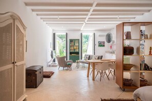 A spacious living area with a sofa, chairs, a dining table, and a bookshelf.