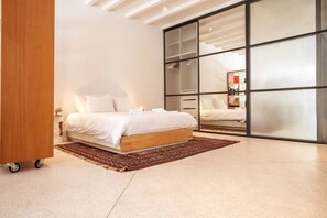 A modern bedroom with a large bed, a sliding glass door, and a wooden cabinet.