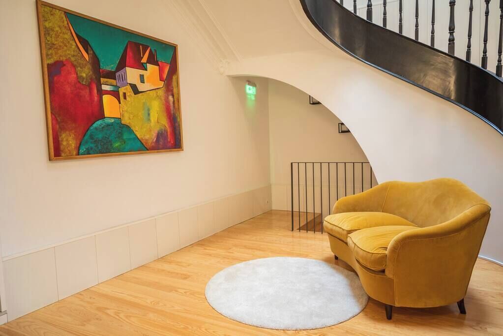 Un interior modern amb un terra de fusta, una armchair groga, una catifa blanca i un quadre abstracte i colorit a la paret.