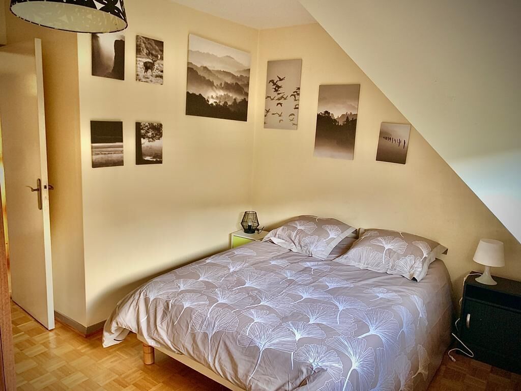 A bedroom with a bed, a nightstand, and a lamp. There are several framed pictures on the wall.