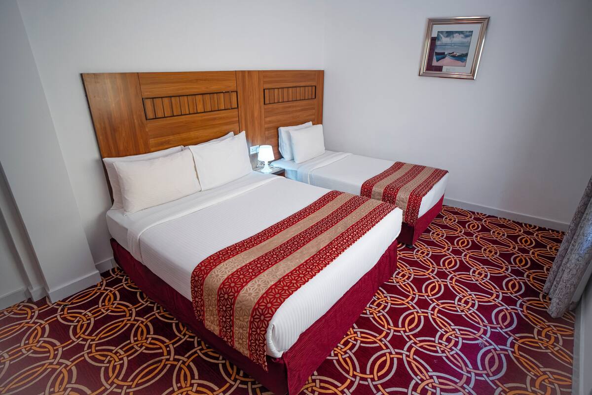 Een hotelkamer met twee bedden, houten hoofdeinden, witte linnens en een kamerbreed tapijt met een patroon.