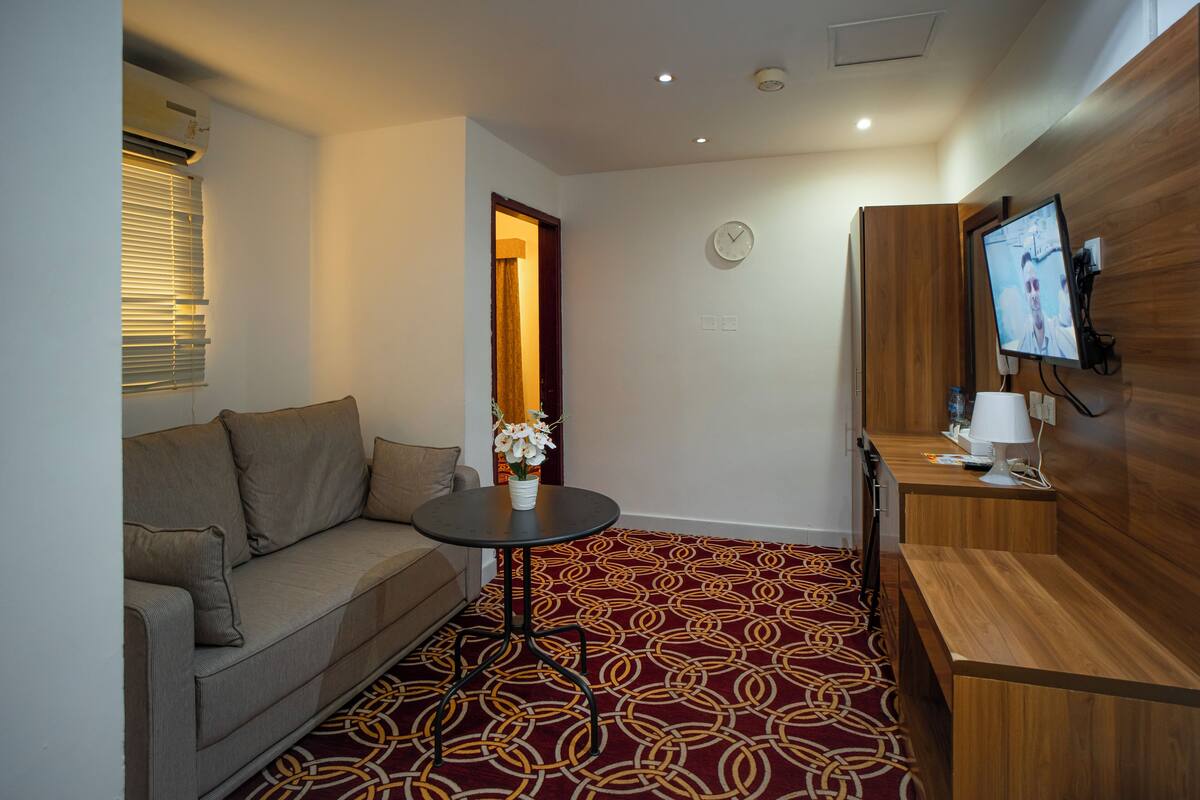 Een hotelkamer met een bank, een kleine tafel met een vaas, een houten bureau, een televisie en een kamerbreed tapijt met dessin.