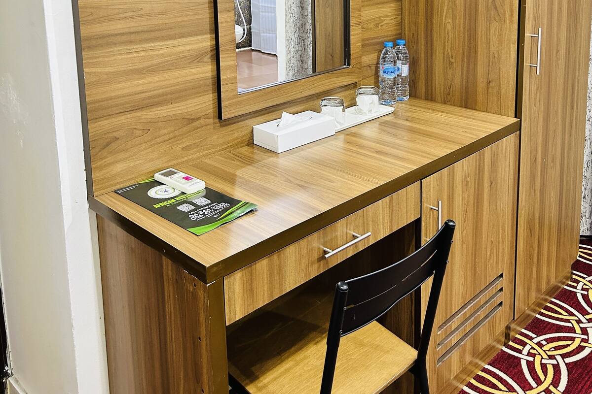 Een houten bureau met een spiegel, een stoel en een klein tafeltje met een zakdoos, een fles en een weegschaal.