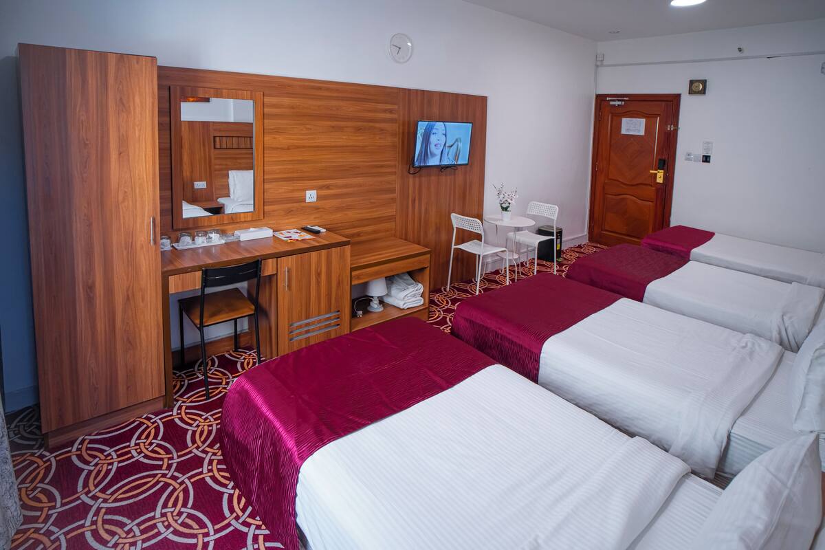 Een hotelkamer met een houten garderobe, een bureau met spiegel, een televisie, een klein tafeltje met stoelen en vier bedden met rode en witte beddengoed.