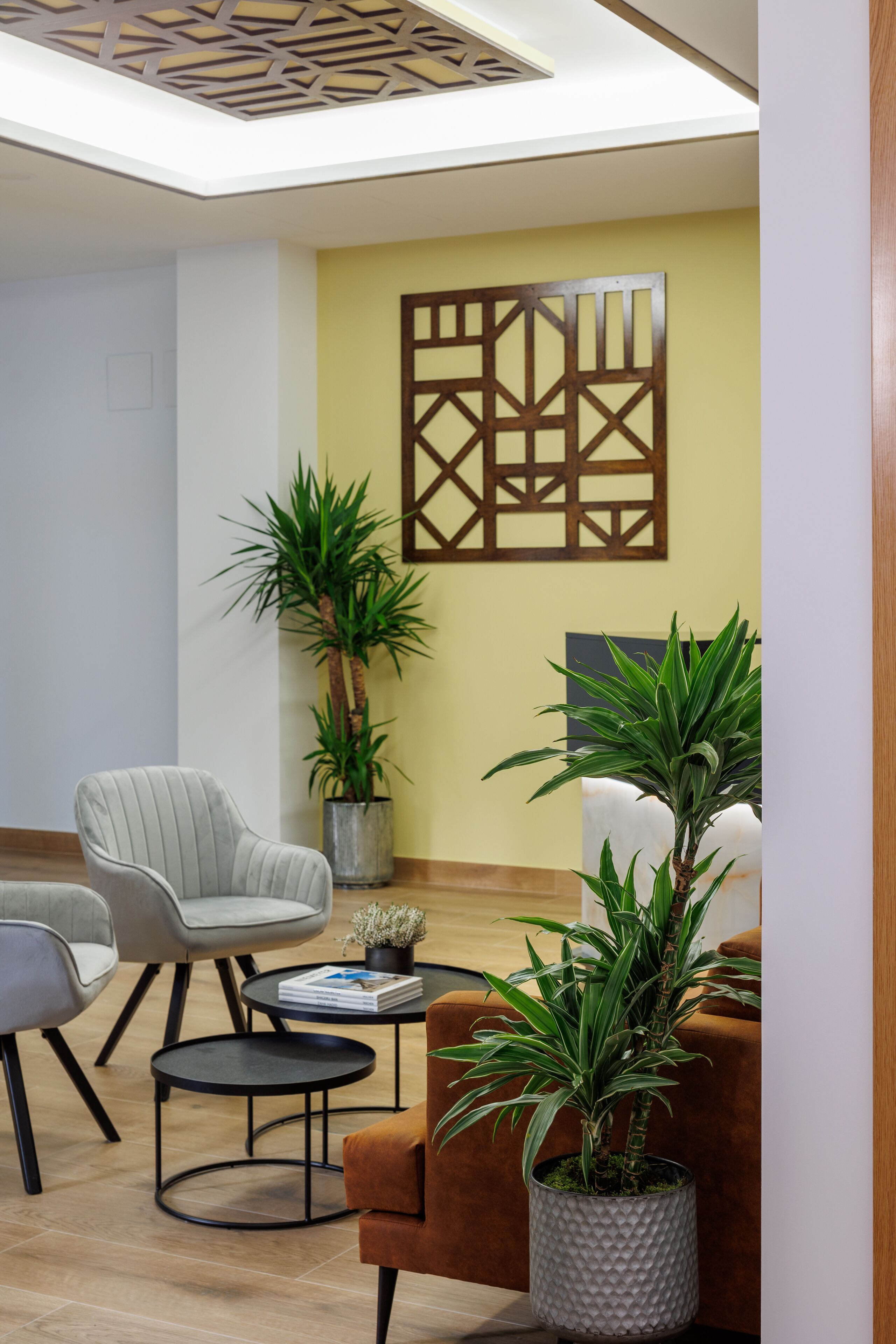 En moderne lobby med siddeområde, to plantekrukker og en dekorativ vægkunst.