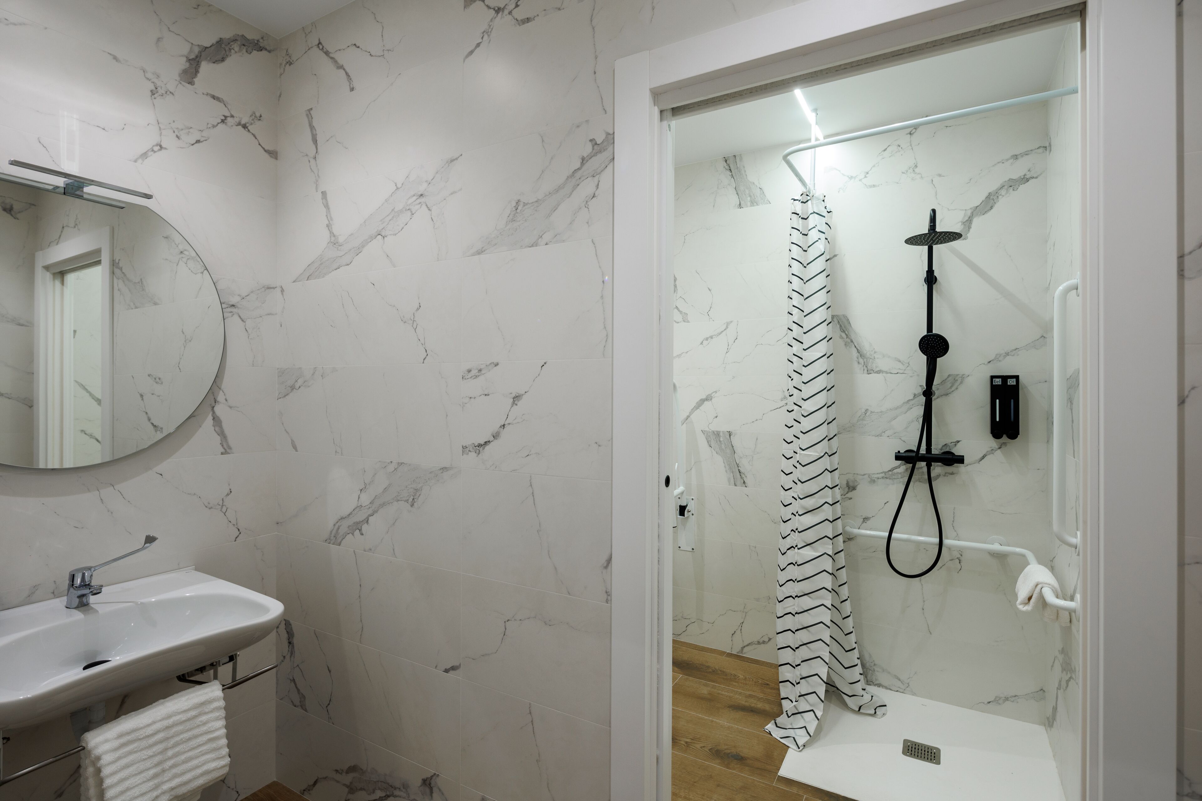 A modern bathroom with a marble backsplash, a sink with a towel, and a glass-enclosed shower with a black hose.