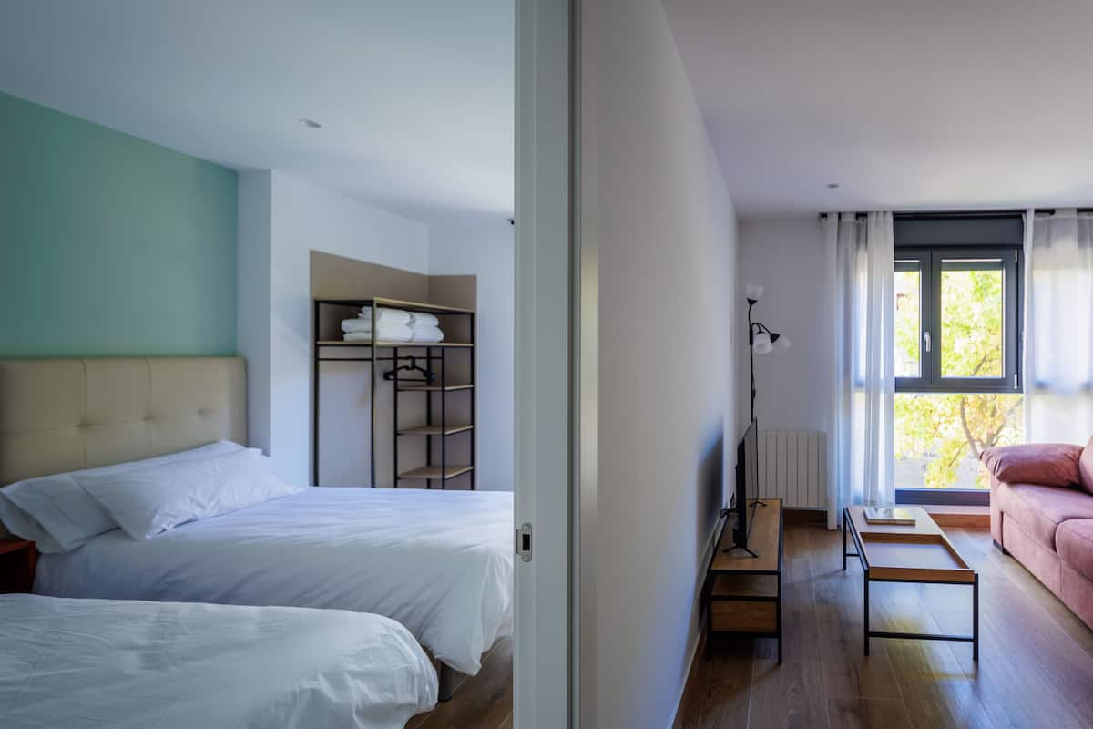 A modern hotel room with two beds, a wardrobe, a desk, and a sofa.