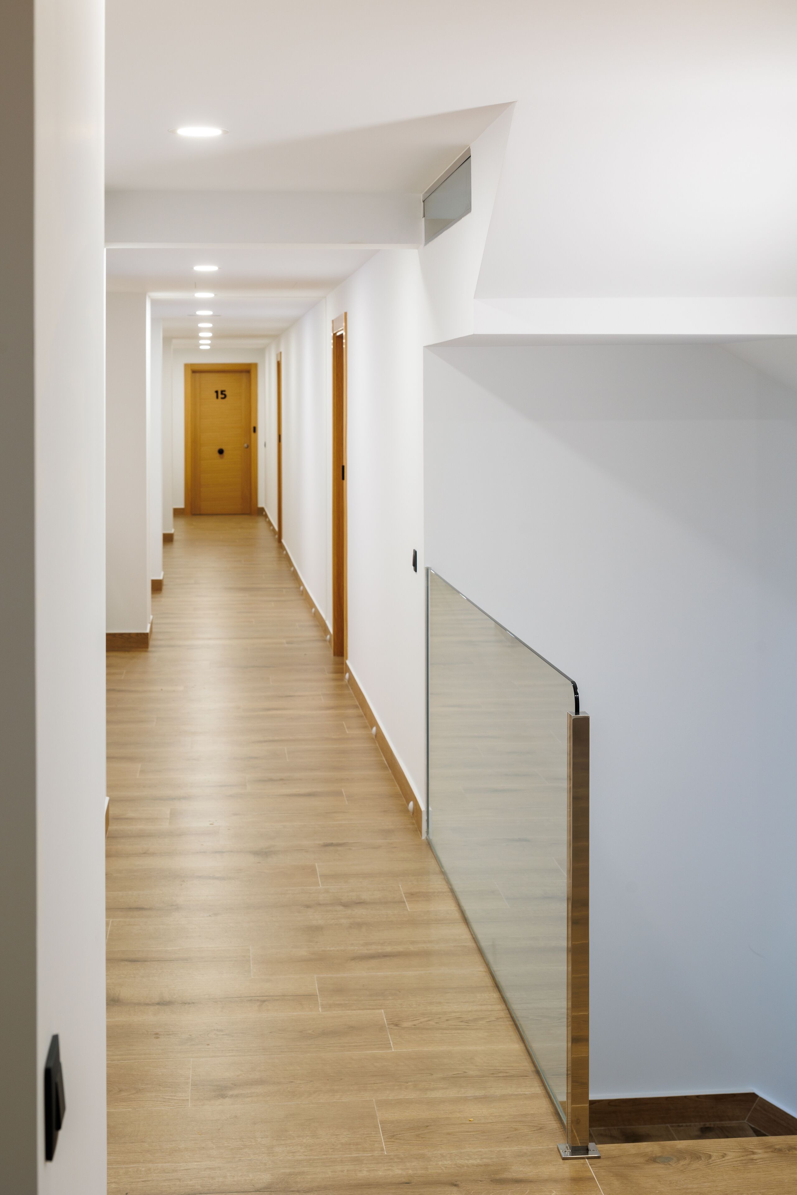 A long, narrow hallway with wooden flooring and white walls.