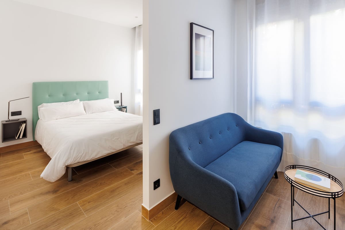 A modern bedroom with a bed, a blue sofa, and a small table with a book.