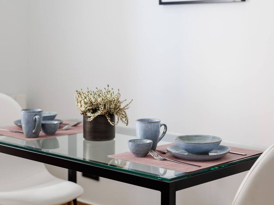 Un coin repas avec une table en verre, des chaises blanches et une œuvre d’art abstraite encadrée accrochée au mur.